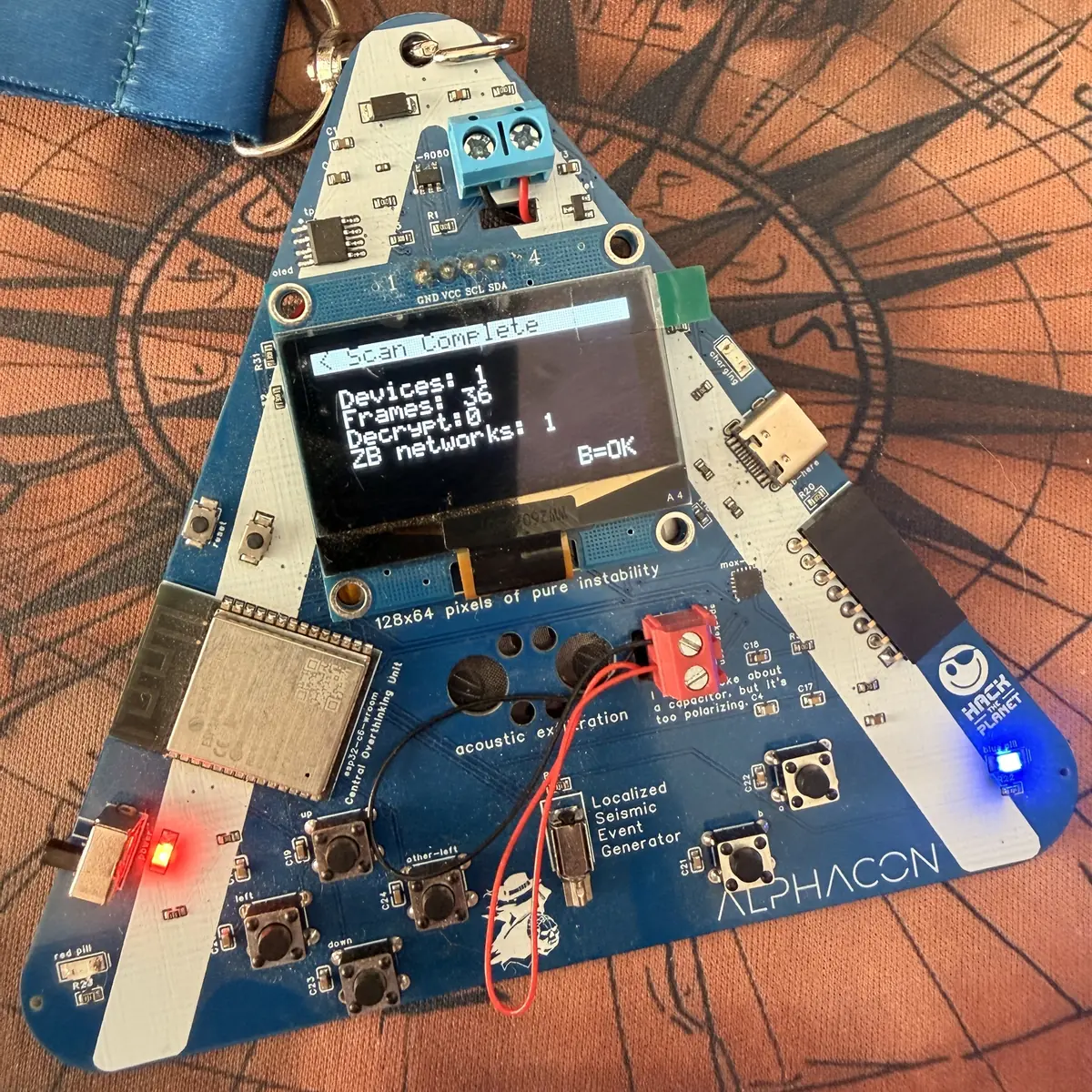 Przód badge'a Alphacon - trójkątna płytka drukowana z wyświetlaczem OLED i modułem ESP32-C6